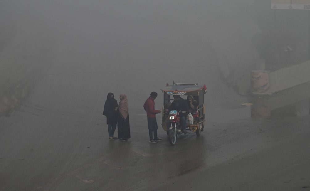 La gente se encuentra junto a una carretera mientras otra conversa con un conductor de moto-rickshaw en medio de una densa niebla tóxica en las afueras de Lahore. Foto: AFP
