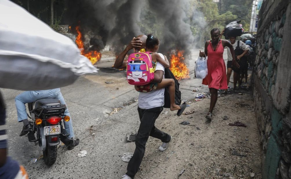 Varias personas corren junto a neumáticos en llamas durante una protesta contra el primer ministro Ariel Henry, el lunes 5 de febrero de 2024, en Puerto Príncipe, Haití. Foto: AP