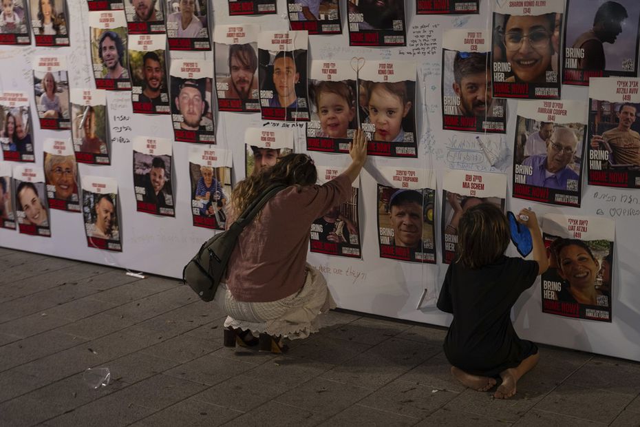 Una mujer israelí toca con la mano fotografías de israelíes desaparecidos y cautivos en Gaza, exhibidas en una pared en Tel Aviv. Foto: AP