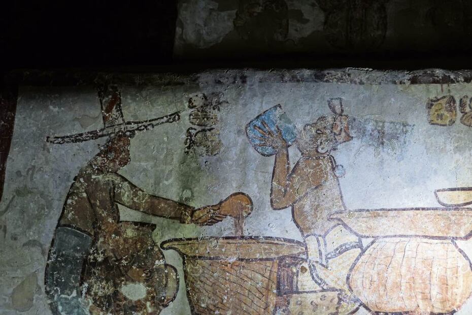 La restauradora Gabriela Mora Navarro explica las escenas del mercado maya plasmadas en una pirámide de Calakmul. En la siguiente imagen (en un recuadro) se observa a un hombre preparando atole y a otro, tomándolo./ Gabriel Pano / El Universal