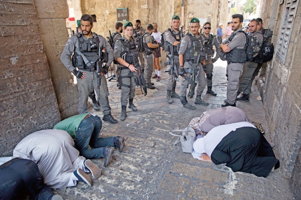Palestinos rezan mientras la policía fronteriza israelí vigila la entrada de la Puerta del León, en la Vieja Ciudad de Jerusalén. (ODED BALILTY. AP)
