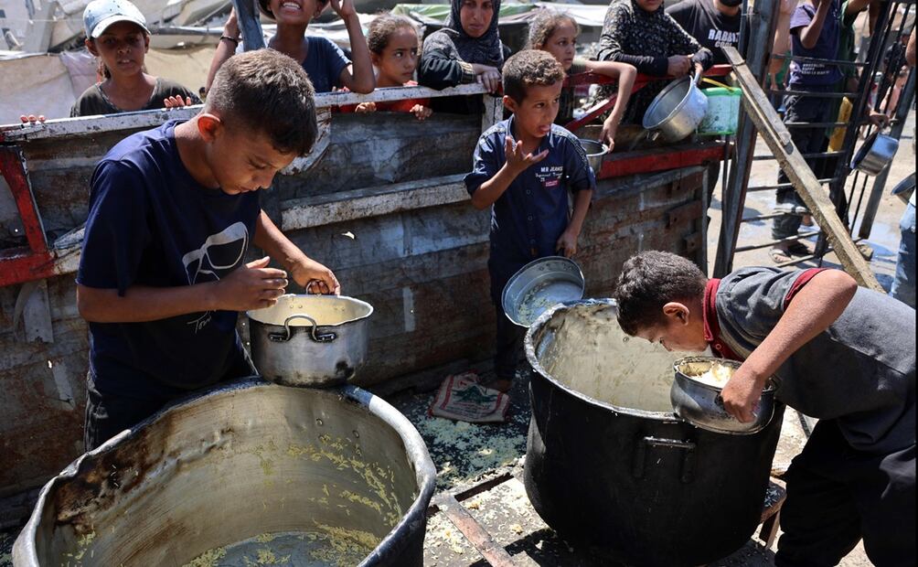 Niños palestinos buscan en ollas vacías un poco de comida en Gaza. Foto: AFP