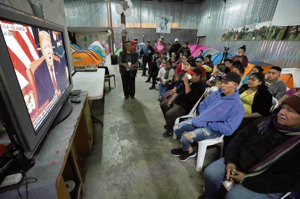 Migrantes, en su mayoría mexicanos y de Centroamérica, reunidos en un albergue en Tijuana, escuchan el discurso de Trump, en el que insistió en tachar de “c r i m i n a les” a quienes entran ilegalmente a EU. (GREGORY BULL. AP)