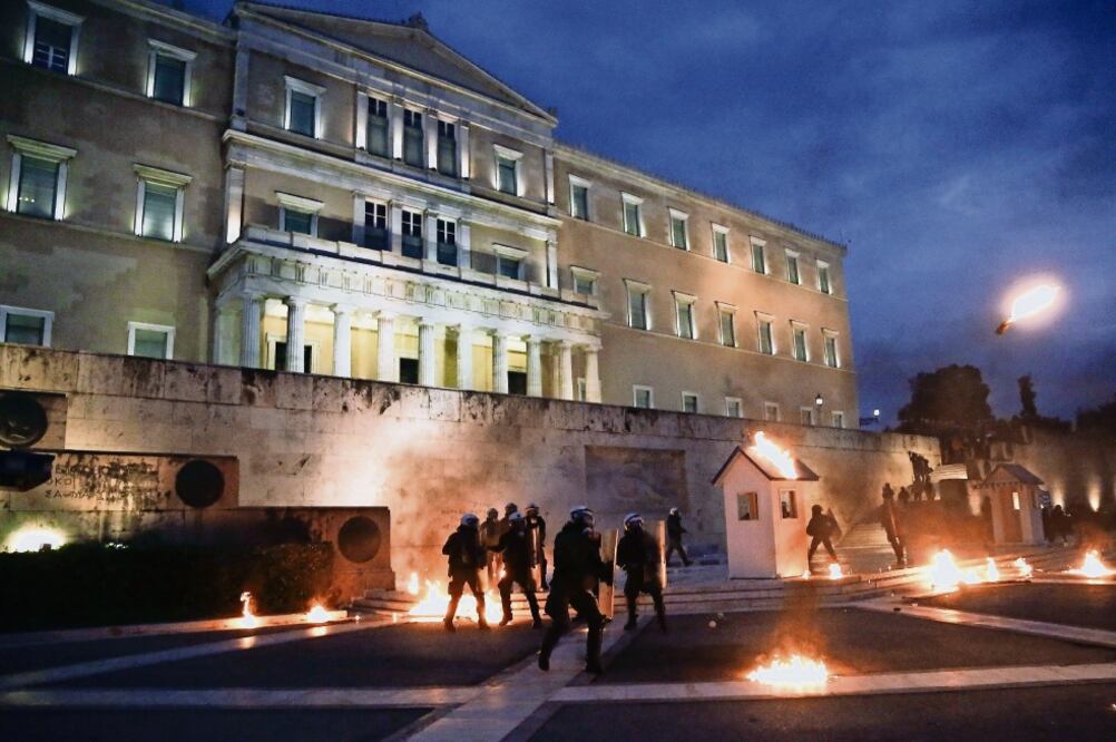 Policías antimotines apostados frente al Parlamento griego se protegen mientras manifestantes les lanzan cócteles molotov, durante las protestas de ayer por la aprobación de nuevas medidas de austeridad (YANNIS KOLESIDIS. EFE)
