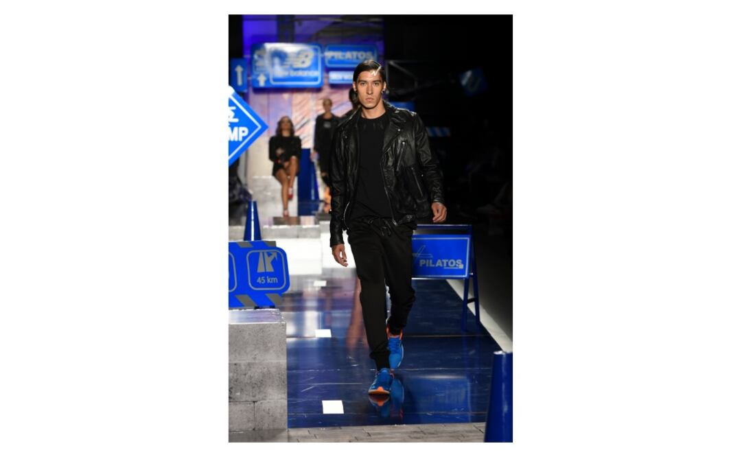 Cazadora estilo biker negra, camiseta negra cuello redondo con estampado de letras, pantalón negro deportivo y tenis New Balance. 