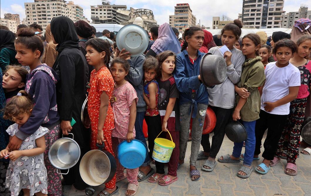 Palestinos, en su mayoría niños, hacen fila frente a un camión de reparto de comida caliente en un campamento de desplazados cerca del puerto de la Ciudad de Gaza. Foto: AFP