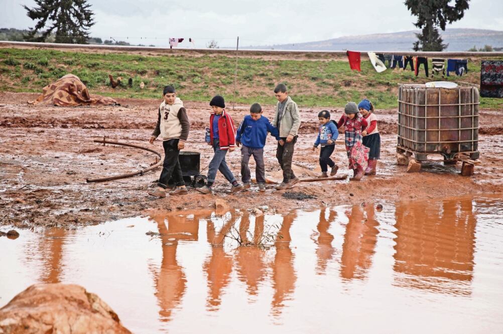 Un grupo de niños sirios caminan en un campo de refugiados cerca de la frontera con Turquía, en el norte de la provincia siria de Idlib. Tras las fuertes lluvias que se han registrado en la zona, el lugar ha sufrido inundaciones. Foto: AAREF WATAD. AFP
