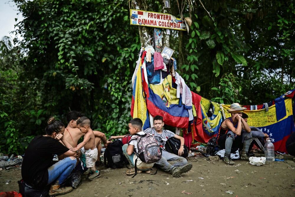Migrantes sentados bajo un cartel que marca la frontera entre Panamá y Colombia durante su viaje a través del Tapón del Darién, en mayo pasado. Foto: AP