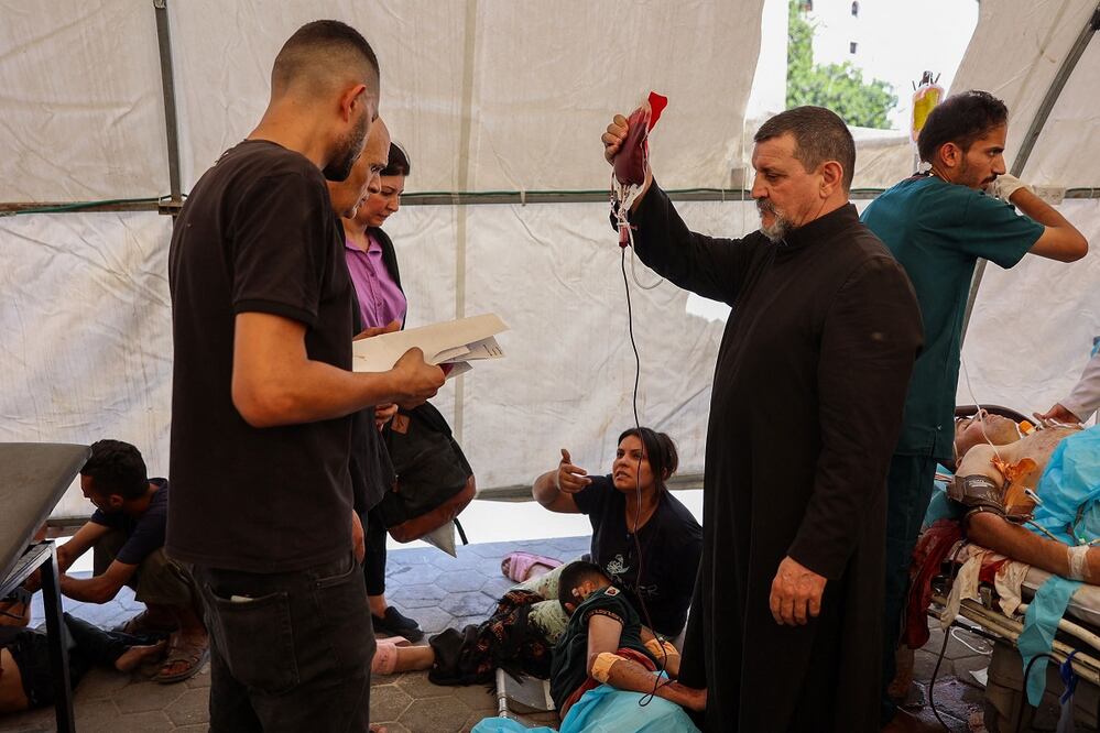 El padre Carlos (centro) de la Iglesia de la Sagrada Familia, en Gaza, auxilia a los heridos por un ataque israelí. FOTO: OMAR AL-QATTAA. AFP