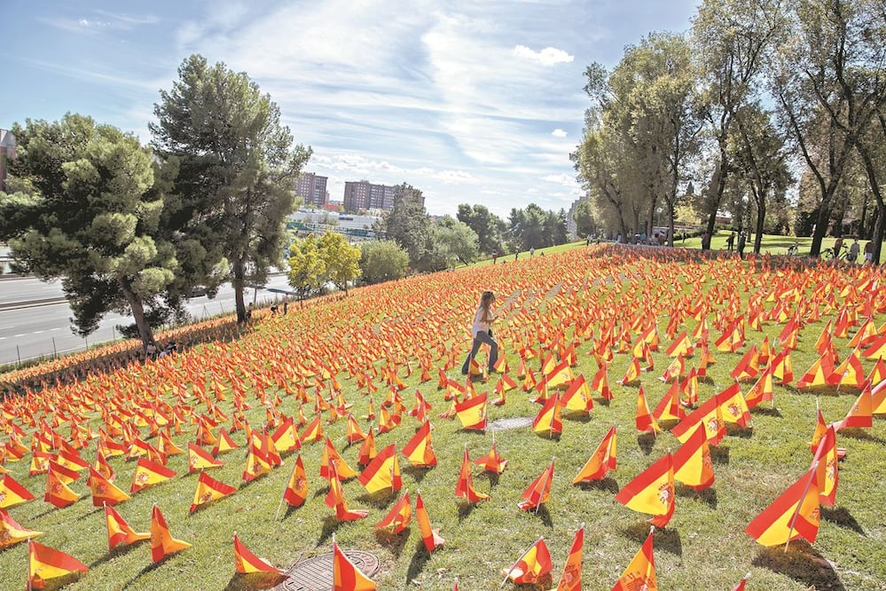 Una mujer camina entre banderas españolas colocadas en Madrid en memoria de los muertos que ha dejado la pandemia por coronavirus en el país, el cual enfrenta un rebrote que obligó a imponer confinamiento selectivo. MANU FERNANDEZ. AP