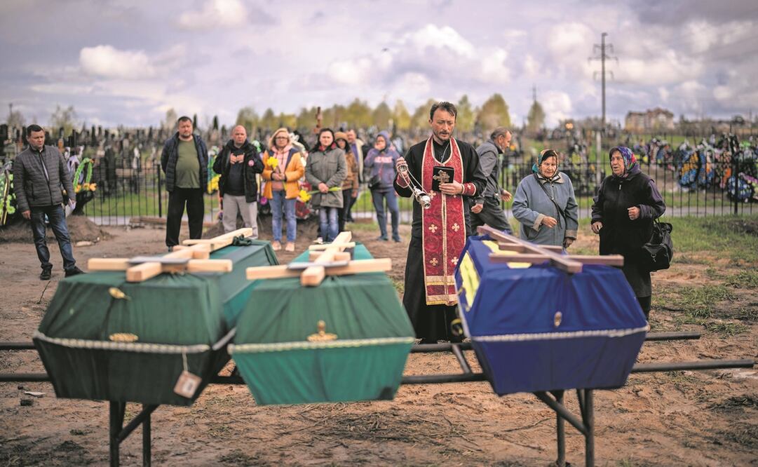 Un sacerdote bendice los cuerpos de tres personas que fallecieron durante la ocupación rusa y fueron desenterradas de las fosas comunes en Bucha.