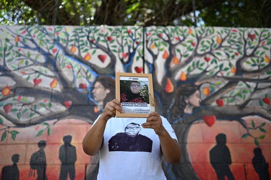Esmeralda Rosales sostiene el retrato de su hermano desaparecido, Fernando Rosales, durante la inauguración de un mural en homenaje a las personas desaparecidas en la Universidad de El Salvador, en San Salvador. La imagen confronta la narrativa oficial de orden y castigo impulsada por el gobierno de Nayib Bukele. Crédito: AFP