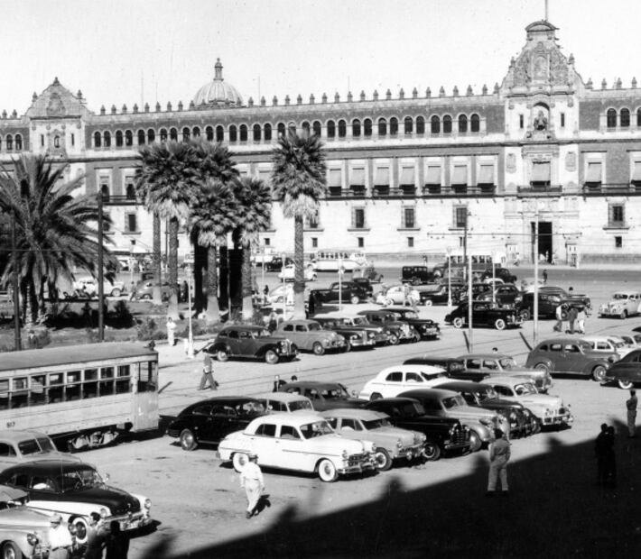 Una toma del Zócalo y el Palacio Nacional hacia finales de los años cuarenta, en la que se aprecia ya con el tercer nivel que le fue añadido en 1926 y que además incluyó la sustitución de la piedra blanca por el tezontle que conocemos. Al frente se aprecian diversos modelos de automóviles estacionados y un tranvía que va pasando; también es notoria la vegetación en la plaza, que a finales de los años cincuenta adoptó su fisonomía actual. Foto: Colección Carlos Villasana/ Especial.