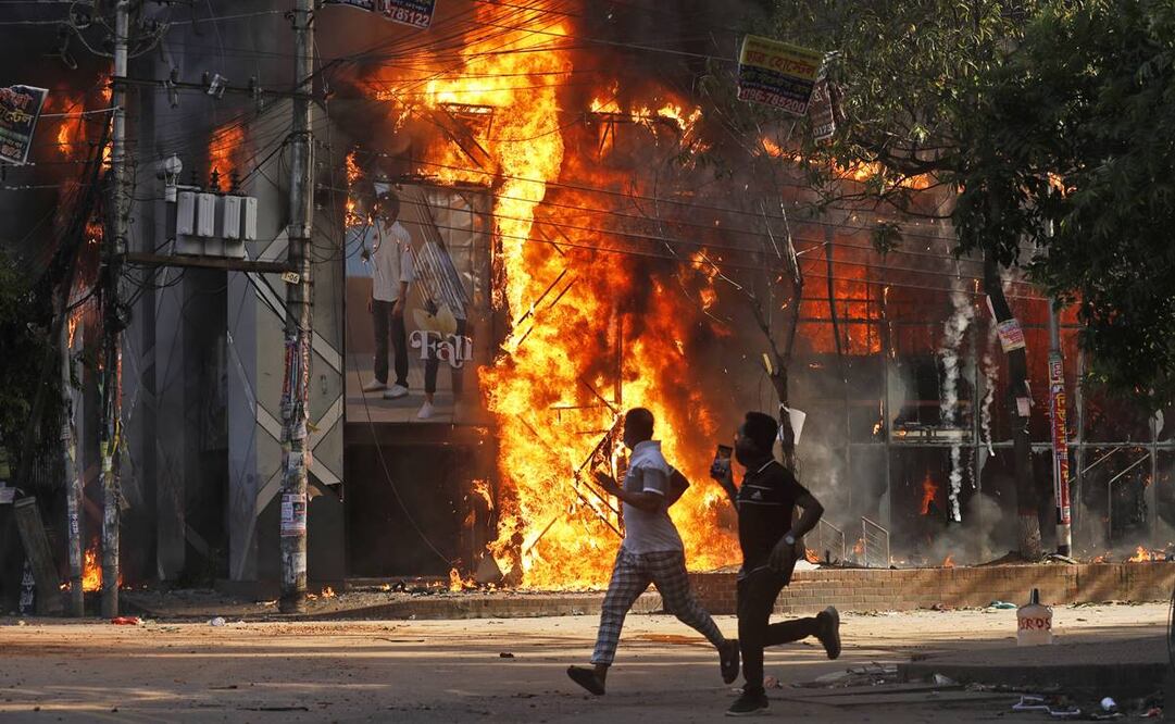 Unos hombres corren frente a un centro comercial que fue incendiado durante una manifestación contra la primera ministra Sheikh Hasina. FOTO: AP