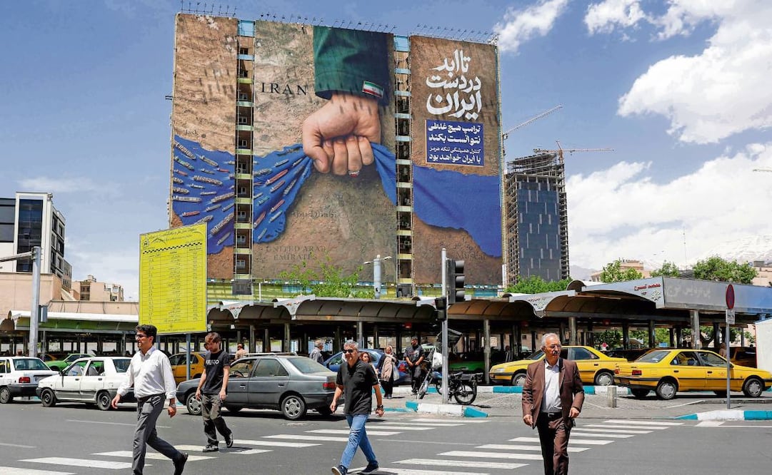 Iraníes cruzan una avenida donde destaca una pancarta que alude al bloqueo en el estrecho de Ormuz. Foto: AFP