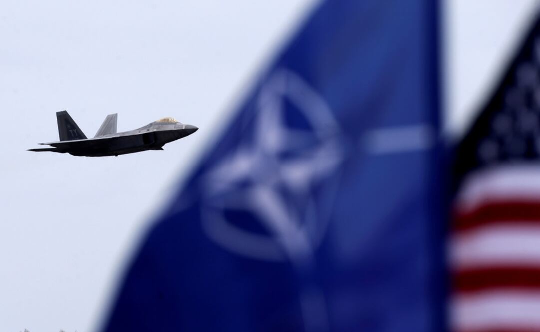 Las banderas de la OTAN y de los Estados Unidos ondean mientras el caza Raptor F-22 de la Fuerza Aérea de los Estados Unidos vuela sobre una base aérea militar - Foto: Ints Kalnins/REUTERS