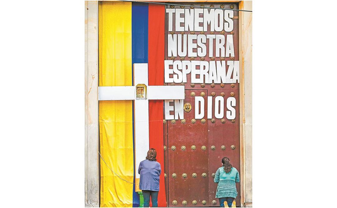 Colombianas rezan frente a una iglesia, cerrada por el Covid-19, en Bogotá. JUAN BARRETO. AFP