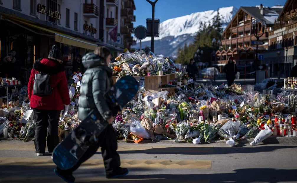 Un joven snowboarder pasa junto a un monumento improvisado con flores, velas y mensajes cerca del bar Constellation en Crans-Montana el 6 de enero de 2026, en honor a las víctimas del incendio que arrasó el local en la lujosa estación de esquí alpino en Nochevieja. Foto: AFP