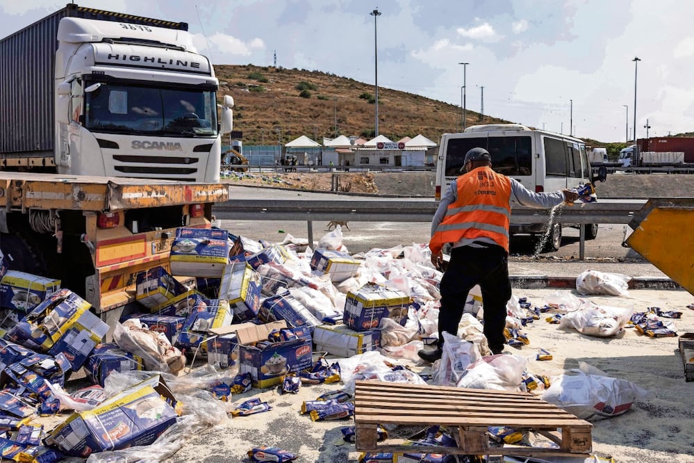 Un trabajador recoge la ayuda que llevaban camiones dañados por israelíes en el cruce de Tarqumiyah. Foto: Oren Ziv | AFP