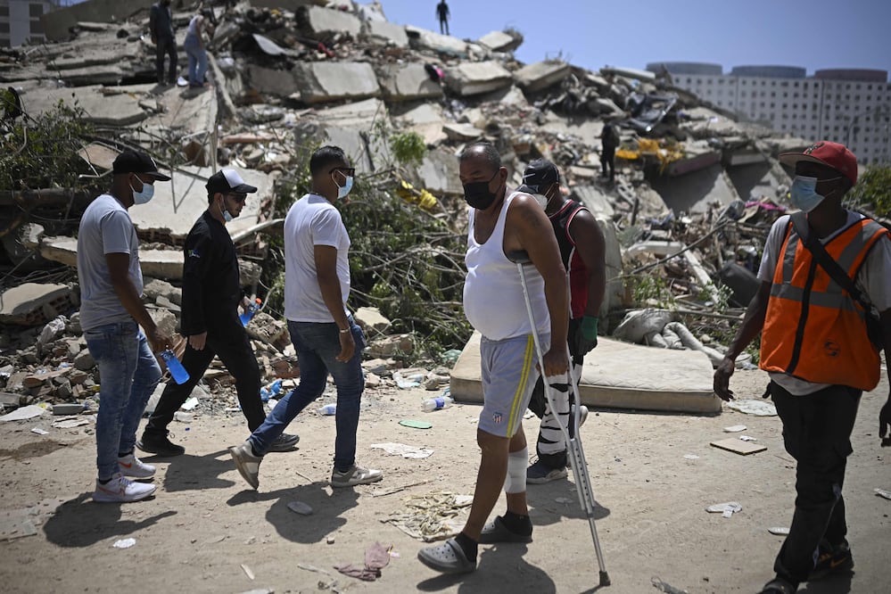 Una persona con muletas pasa frente a voluntarios que trabajan junto a un edificio derrumbado en La Guaira (27/06/2026). Foto: AFP