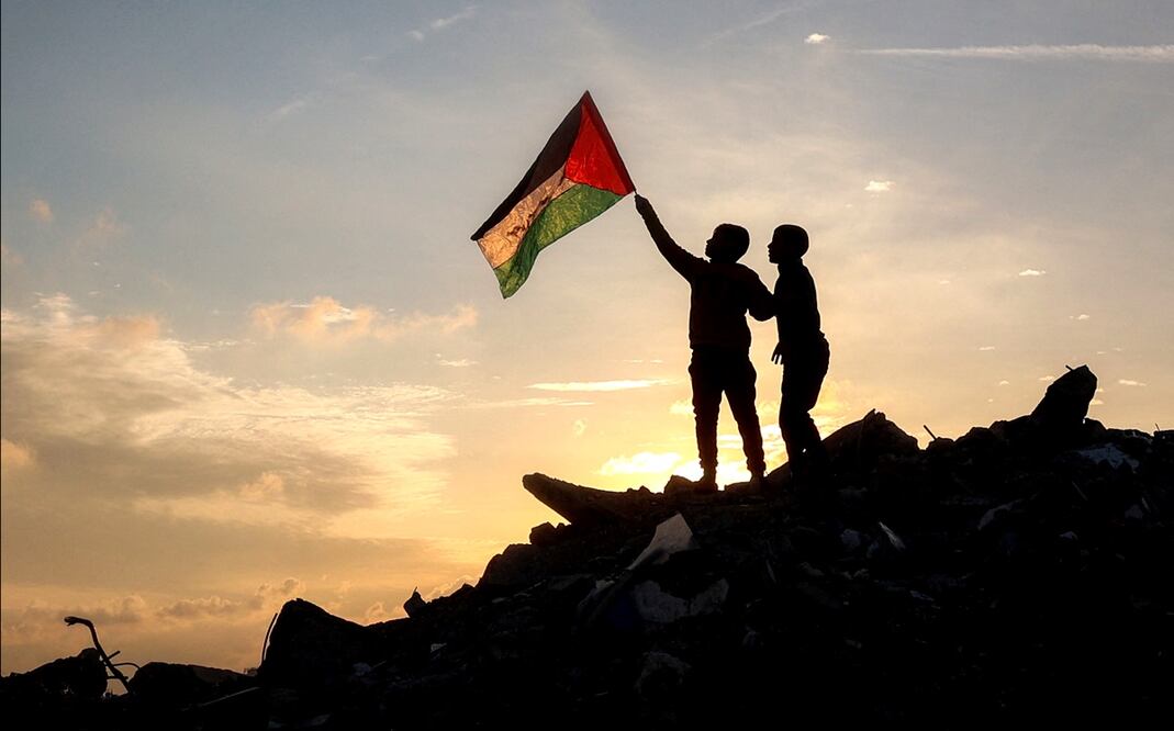 Un par de niños ondean una bandera palestina sobre un montón de escombros en un campamento para desplazados en la Franja de Gaza. Foto: AFP
