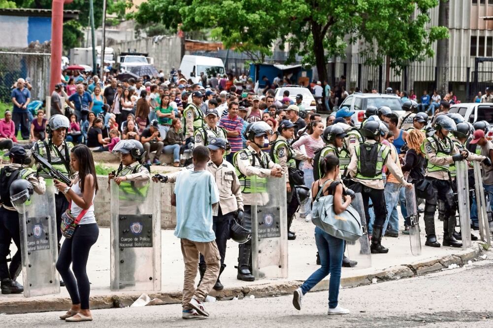 Policías custodian el orden en Caracas, ayer, mientras venezolanos esperan para entrar a un supermercado. La escasez de productos desató protestas (MIGUEL GUTIÉRREZ. EFE)