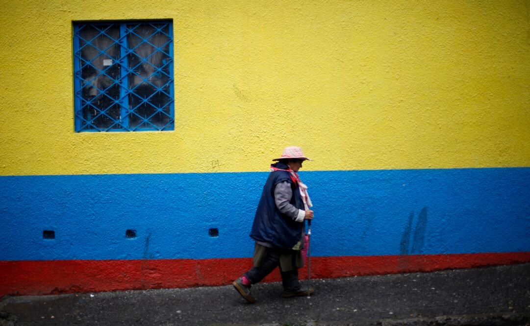 A Colombian woman walks in front of a wall painted in the colours of the Colombian flag in Bogotá - Photo: Eliana Aponte/REUTERS