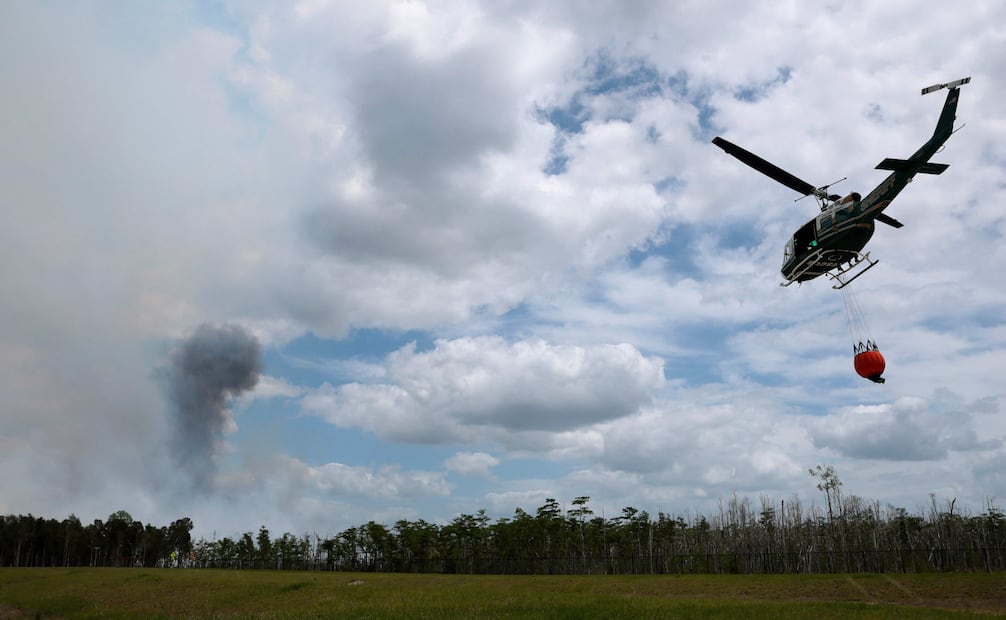 Un helicóptero descarga agua sobre el incendio forestal mientras una columna de humo se eleva en el suroeste de Florida. Foto: AFP.