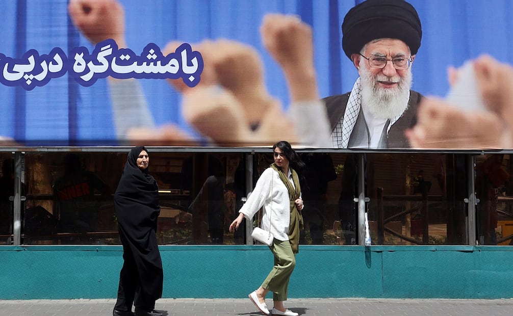 Mujeres iraníes pasan junto a un gran cartel del difunto líder supremo iraní, el ayatolá Ali Jamenei, antes de su funeral en Teherán, Irán (02/07/2026). Foto: EFE