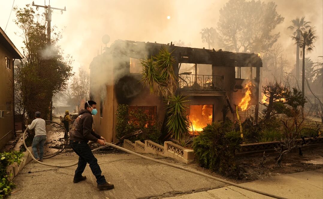 Personas ayudan a un bombero a estirar una manguera mientras un edificio de apartamentos se incendia, el miércoles 8 de enero de 2025, en la sección Altadena de Pasadena, California. Foto AP/Archivo