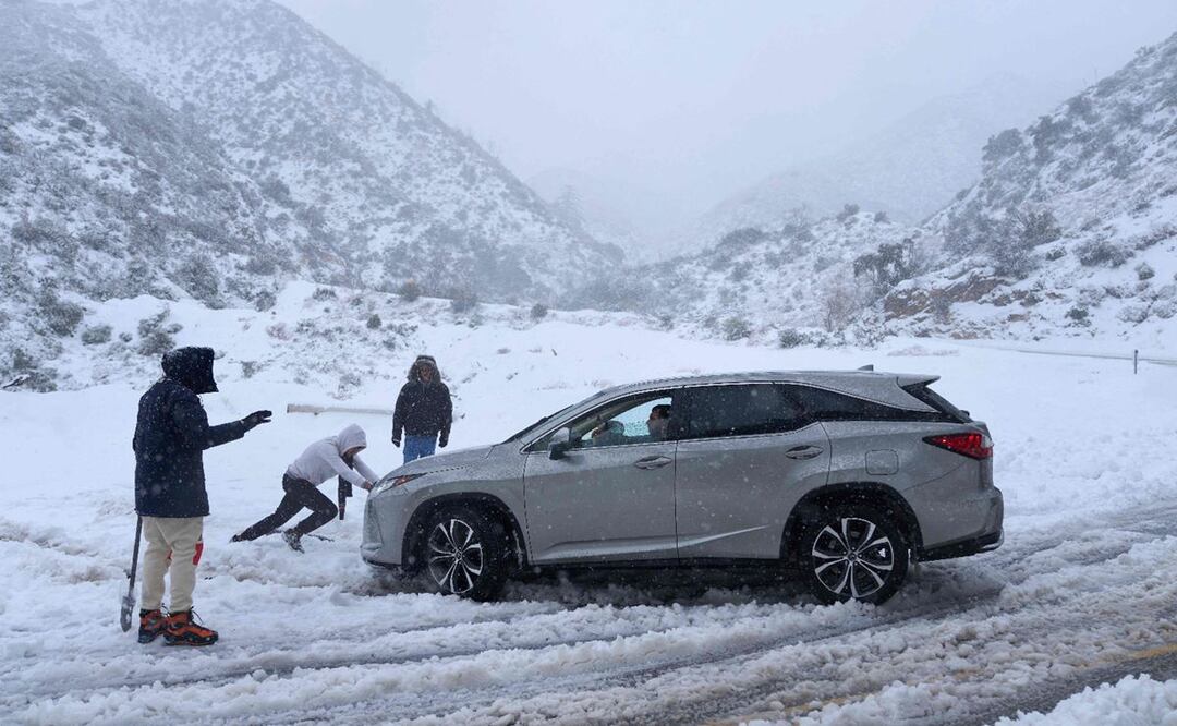 Una persona ayuda a sacar un vehículo que quedó atascado en la nieve en una carretera en las montañas de San Gabriel en el Bosque Nacional Ángeles. FOTO: AFP