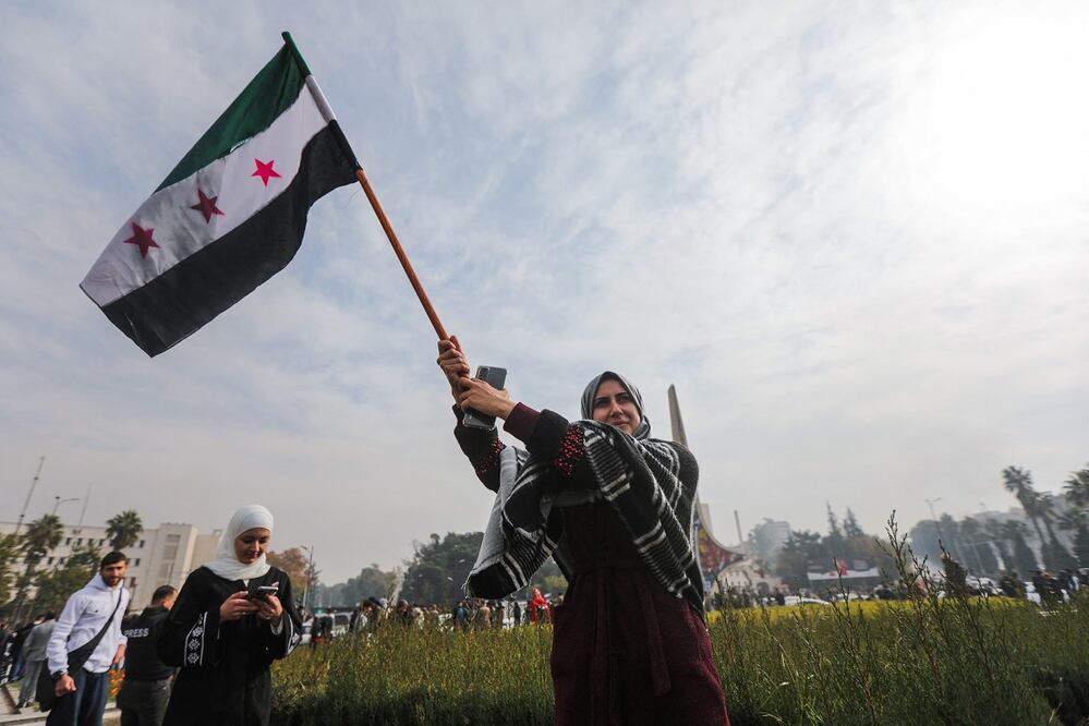 Una mujer ondea una bandera de la oposición siria mientras celebra en la plaza de los Omeyas en Damasco la caída de Bashar al-Assad. FOTO: BAKR ALKASSEM. AFP