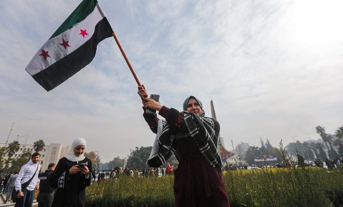 Una mujer ondea una bandera de la oposición siria mientras celebra en la plaza de los Omeyas en Damasco la caída de Bashar al-Assad. FOTO: BAKR ALKASSEM. AFP