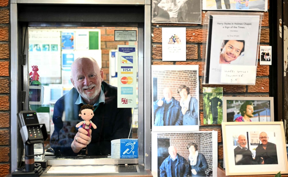 El jefe de estación, Graham Blake, sostiene un muñeco de ganchillo de Harry Styles mientras posa rodeado de imágenes del cantante en la estación de tren de Holmes Chapel, al noroeste de Inglaterra. 
Foto de Oli SCARFF / AFP.