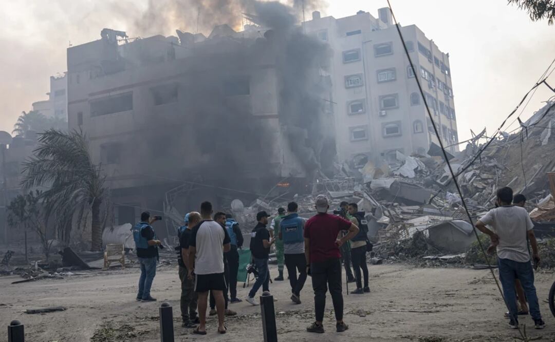 En esta imagen de archivo, reporteros observan mientras palestinos inspeccionan un edificio alcanzado por un bombardeo israelí en la Ciudad de Gaza. Foto: AP