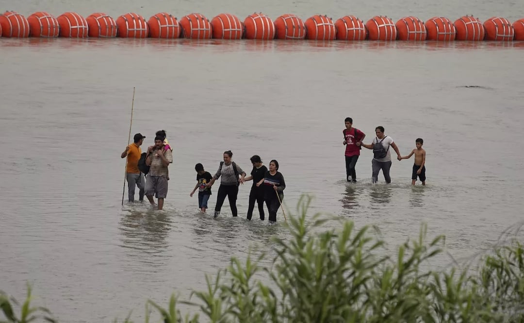 Migrantes que cruzaron el río Grande (Bravo) desde México caminan frente a enormes boyas colocados como una barrera fronteriza flotante en el río. Foto: AP