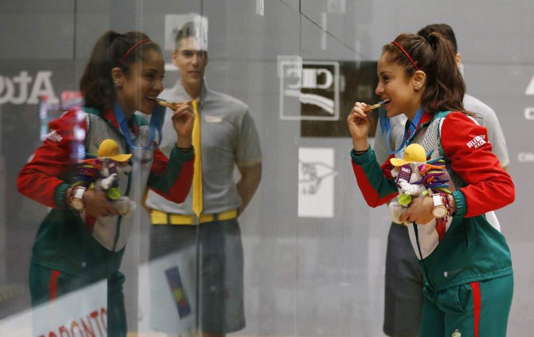 Ante su reflejo en el cristal, Paola Longoria, quien hizo efectivo el pronóstico, presume una de las dos medallas de oro conseguidas ayer en racquetbol, a la que le dio un mordisco (JULIO CORTEZ. AP)