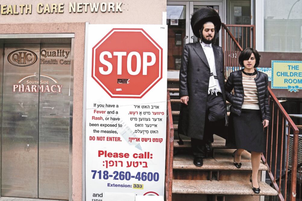 Alerta. Un judío ultraortodoxo camina al lado de una pancarta que avisa por el brote de sarampión en Brooklyn, Nueva York. / CARLO ALLEGRI. REUTERS