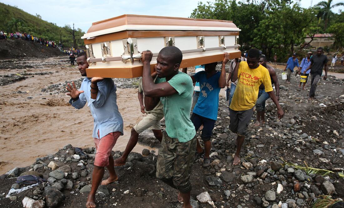 Varios hombres cargan un ataúd e intentan cruzar el río La Digue, debido al derrumbe del único puente que conecta con el sur, tras el paso del huracán Matthew (Foto: EFE)