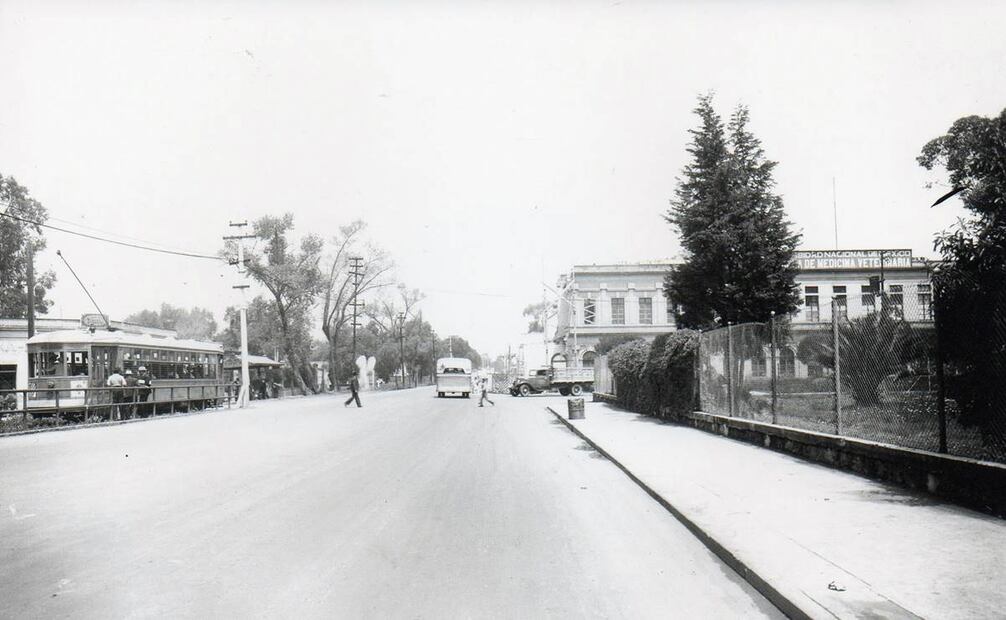 La Calzada México-Tacuba y el cruce con la avenida Maestro Rural alrededor de 1940. A la derecha está la Escuela de Medicina Veterinaria, cuya fachada fue recortada para ampliar la vialidad; este edificio inició su construcción en la década de 1880 y más tarde albergó la Secundaria 96. A la izquierda se ve una parada del tranvía, muy cerca del actual Metro Colegio Militar. Imagen: Colección David Guerrero.
