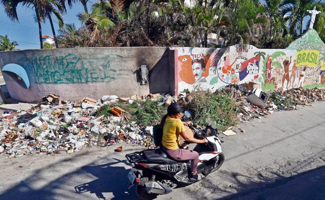 Cubanos pasan por una calle de La Habana llena de basura que se acumula debido a que no hay gasolina para que los camiones pasen a recoger desechos. Foto: Ernesto Mastrascusa / EFE