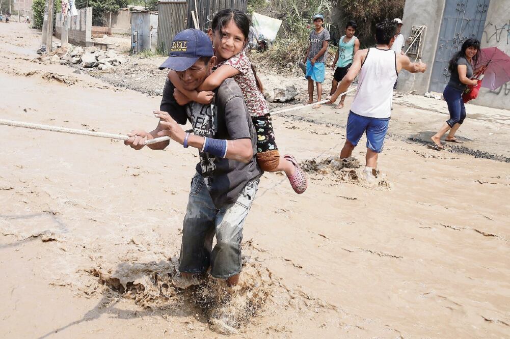 Peruanos cruzan una calle inundada sujetándose de una cuerda, tras el desbordamiento del río Rimac, en la zona de Carapongo, en Huachipa, en la provincia de Lima, desde hace semanas por intensas lluvias. (XINHUA)