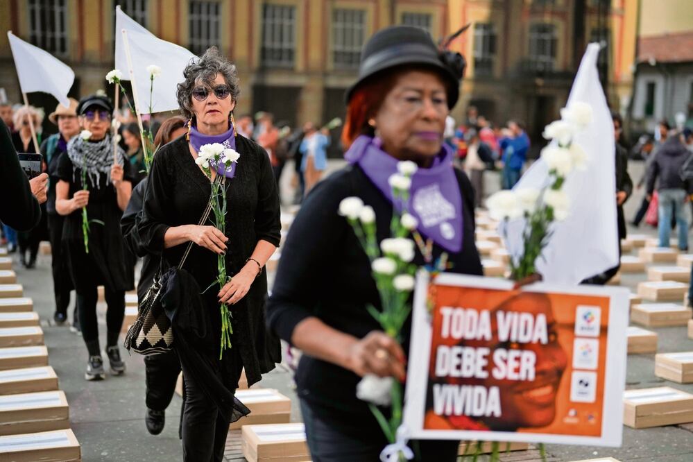 Colombianas sostienen flores y caminan entre cajas que representan ataúdes simbólicos, mientras recuerdan a exguerrilleros y líderes sociales en Bogota. Foto: de Fernando Vergara. AP