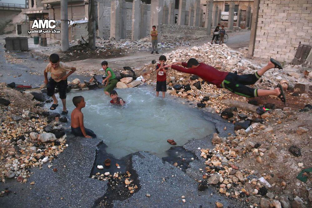Niños nadan en un agujero lleno de agua, creado por un misil en la ciudad siria de Aleppo (Foto: AP)