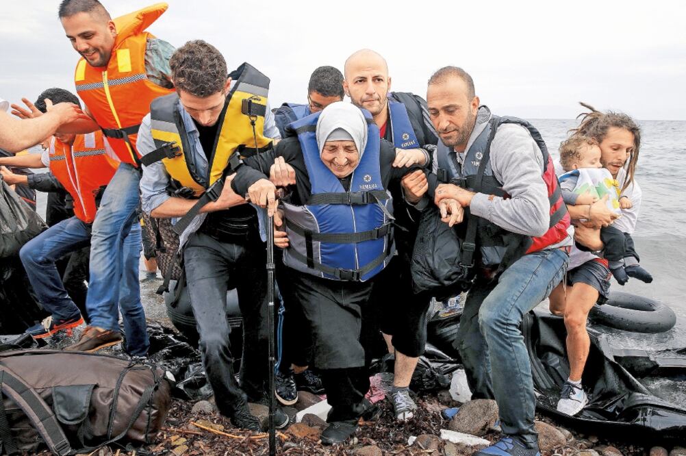 Refugiados sirios ayudan a una anciana proveniente de la costa turca a desembarcar, tras llegar a la isla griega de Lesbos, ayer (YANNIS BEHRAKIS. REUTERS)