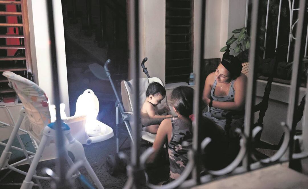 Una cubana, con sus hijos en el portal de su casa, bajo la luz de una lámpara, durante un apagón en La Habana. La falta de electricidad es una de las razones de las más recientes protestas contra el régimen de la isla. Foto: Ernesto Mastrascusa/EFE