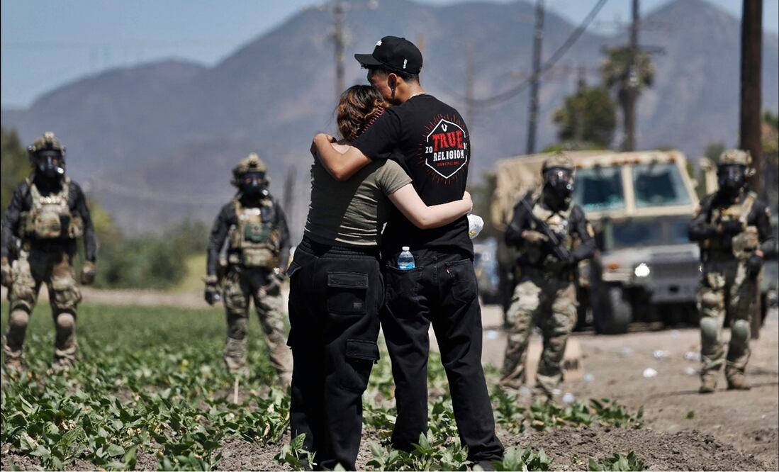 Un hombre y una mujer se abrazan frente a agentes federales durante una redada de inmigración del ICE en una granja de cannabis con licencia cerca de Camarillo, California, el 10 de julio de 2025. Foto: AFP