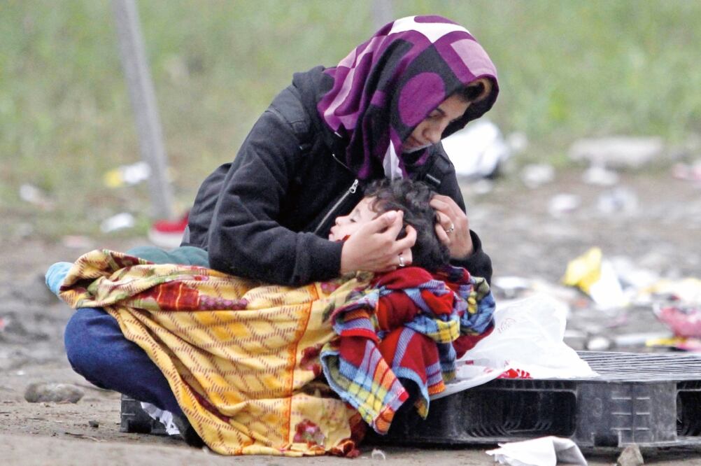 Una mujer intenta mantener caliente a su hijo, mientras espera para entrar al campamento para refugiados de Gevgelija, en Macedonia (BORIS GRDANOSKI. AP)