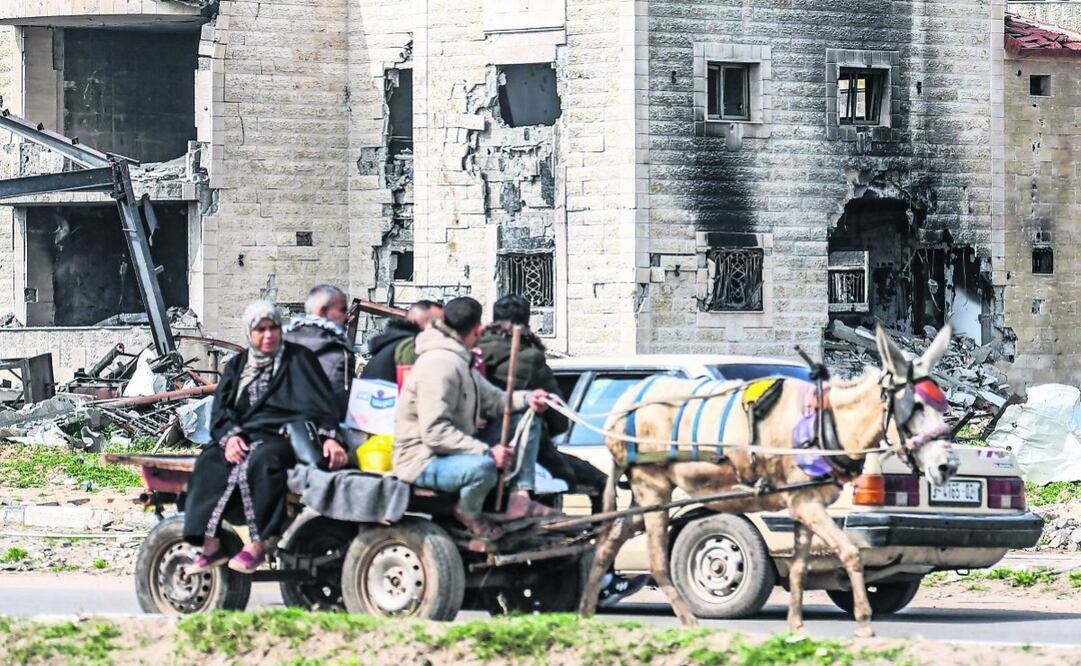 Palestinos en una carreta tirada por un burro frente a las ruinas de un edificio en el campamento de refugiados de Maghazi, dañado por los bombardeos israelíes en medio del conflicto en la Franja de Gaza. Foto: AFP