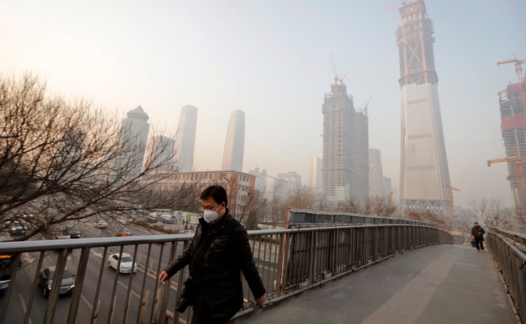 Un hombre que tiene una mascarilla para protegerse de la contaminación del aire camina por un puente peatonal en Beijing / AP